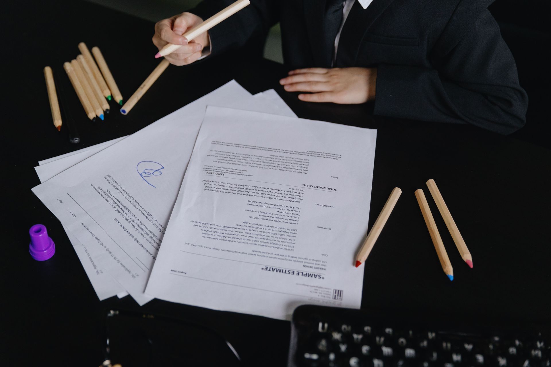 A business professional in formal attire reviews documents with colored pencils at a desk.